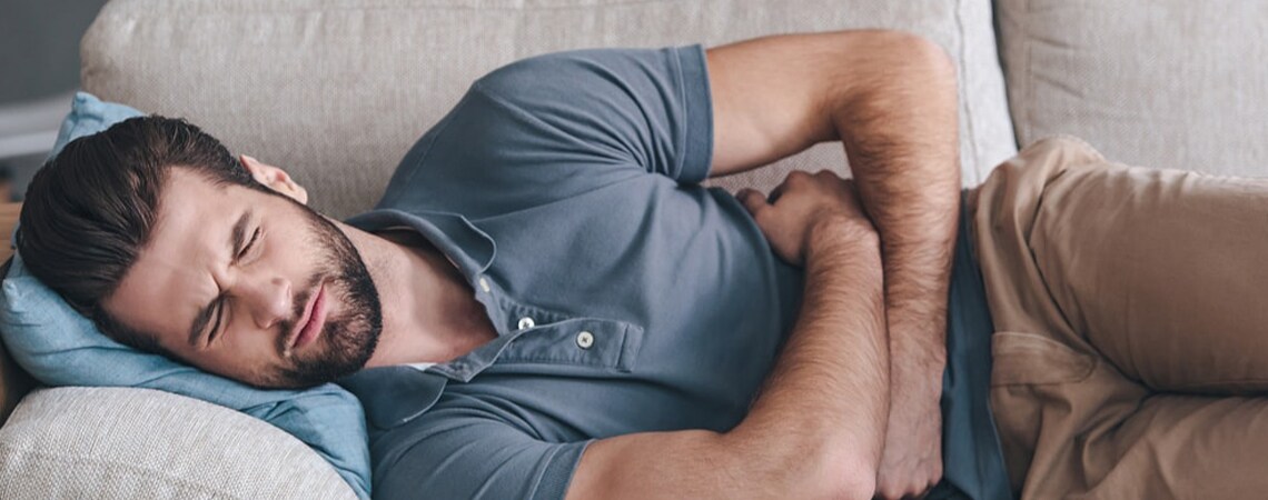 Moški, ki trpi zaradi sindroma razdražljivega črevesja, leži na boku in se v bolečinah drži za trebuh.